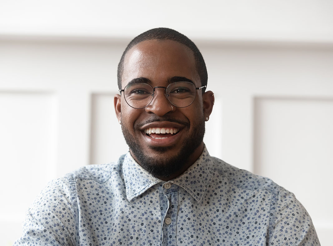 Image of a young black man smiling.  He is wearing glasses, and a blue floral shirt.  His head and shoulders are in view.